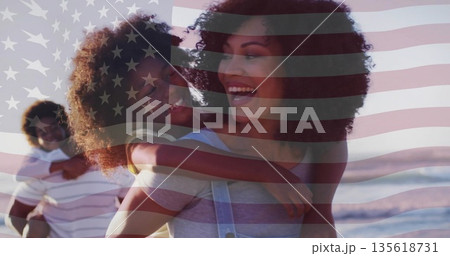 Parents giving piggyback rides on sandy beach, with American flag overlay and ocean waves Parents giving piggyback rides on sandy beach, with American flag overlay and ocean waves 135618731