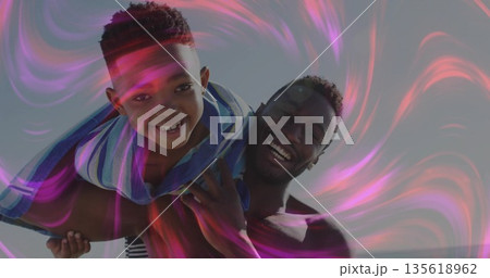 Father carrying son piggyback outdoors, with striped towel and pink purple light swirls 135618962