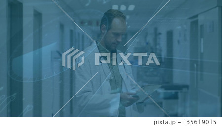 Reading clipboard male doctor standing hospital corridor under lights, holding stethoscope by cart Reading clipboard male doctor standing hospital corridor under lights, holding stethoscope by cart 135619015