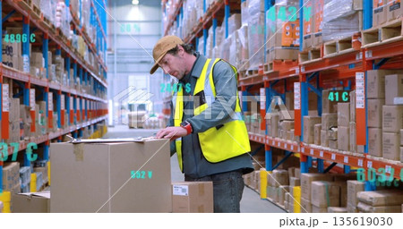 Inspecting warehouse worker in hivis vest leaning over box using clipboard in aisle, shelving racks Inspecting warehouse worker in hivis vest leaning over box using clipboard in aisle, shelving racks 135619030