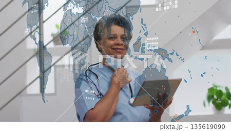 Reviewing nurse in scrubs holding tablet, adjusting mask strap in clinic with world map overlay Reviewing nurse in scrubs holding tablet, adjusting mask strap in clinic with world map overlay 135619090