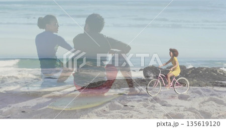 Cycling woman in yellow dress on pink bike along beach overlaying couple on surfboard, copy space 135619120