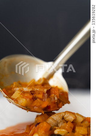 白モツのトマト煮込みをお玉で皿に盛り付ける 135619282