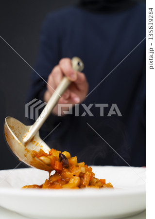 白モツのトマト煮込みをお玉で皿に盛り付ける 白モツのトマト煮込みをお玉で皿に盛り付ける 135619284