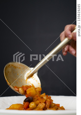 白モツのトマト煮込みをお玉で皿に盛り付ける 白モツのトマト煮込みをお玉で皿に盛り付ける 135619285