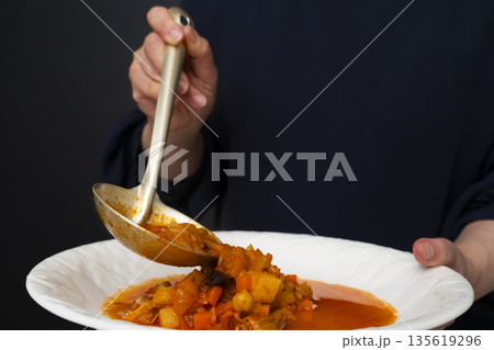 白モツのトマト煮込みをお玉で皿に盛り付ける 白モツのトマト煮込みをお玉で皿に盛り付ける 135619296