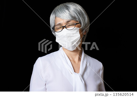 マスクをして辛そうに眉間にシワを寄せる白髪のシニア女性 135620514