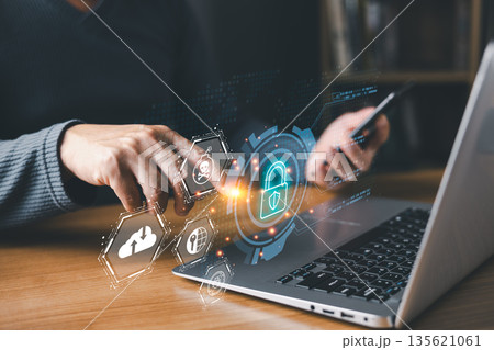 person using a laptop and smartphone interacts with glowing digital icons of a lock, shield, and skull, symbolizing cybersecurity, online protection, data security, and defense against cyber threats. person using a laptop and smartphone interacts with glowing digital icons of a lock, shield, and skull, symbolizing cybersecurity, online protection, data security, and defense against cyber threats. 135621061