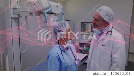 Doctor and nurse analyzing X-ray scan under ceiling-mounted tube in radiology, wearing stethoscopes 135623101