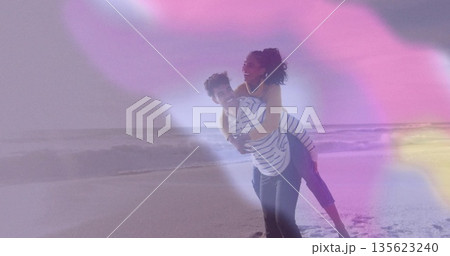 Giving piggyback ride couple in casual wear at shoreline with lapping ocean waves, pastel flares 135623240