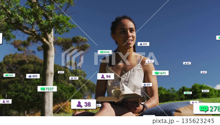 Reading woman wearing fitness watch, striped sundress in park, open book, cushion, digital overlays 135623245
