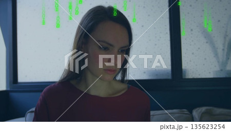 Woman wearing burgundy top sitting in dimly lit room, with sofa, rainy window and green code 135623254