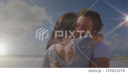 Hugging couple holding each other on sandy beach at sunset, sunlight reflecting off ocean waves Hugging couple holding each other on sandy beach at sunset, sunlight reflecting off ocean waves 135623259