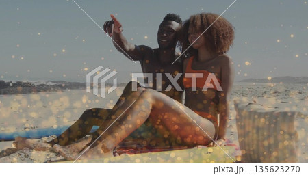 Shirtless man pointing at horizon on beach towel, bikini woman sitting by surfboard and basket Shirtless man pointing at horizon on beach towel, bikini woman sitting by surfboard and basket 135623270