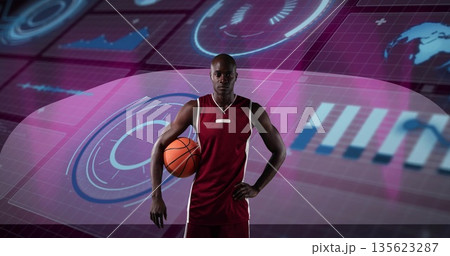 Holding basketball, male athlete standing center in data studio with HUD projections, data charts Holding basketball, male athlete standing center in data studio with HUD projections, data charts 135623287