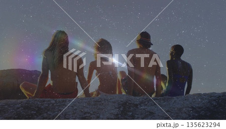 Shirtless men and bikini-wearing women friends admiring night sky on rocky ledge, with lens flare Shirtless men and bikini-wearing women friends admiring night sky on rocky ledge, with lens flare 135623294