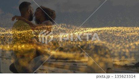 Kissing romantic couple on metal railing at sandy beach and ocean waves, golden light scattering 135623314