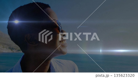 Standing woman wearing blue striped shirt facing sea at seaside, with dark sunglasses, copy space Standing woman wearing blue striped shirt facing sea at seaside, with dark sunglasses, copy space 135623320
