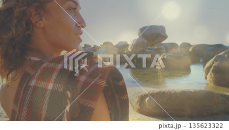 Woman wrapped in plaid blanket gazing at boulders on shoreline, with necklace and pools, copy space Woman wrapped in plaid blanket gazing at boulders on shoreline, with necklace and pools, copy space 135623322
