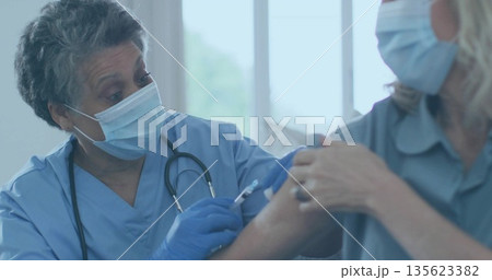 Injecting nurse administering vaccine to patient at clinic, with syringe, gloves, mask, copy space 135623382