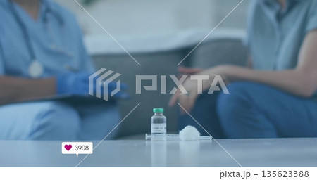 Showing vial labeled COVID-19 on table in lounge, with clinician in scrubs noting syringe tray Showing vial labeled COVID-19 on table in lounge, with clinician in scrubs noting syringe tray 135623388