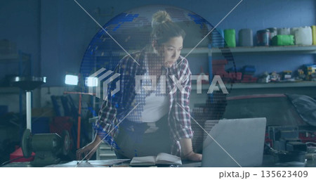 Leaning Asian woman mechanic wearing plaid shirt, jeans, checking laptop in garage, with car engine Leaning Asian woman mechanic wearing plaid shirt, jeans, checking laptop in garage, with car engine 135623409