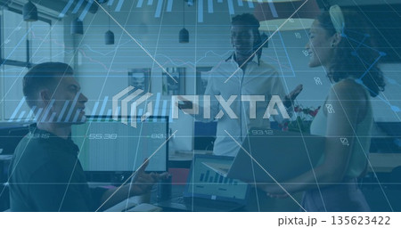 Discussing data among three colleagues in business attire in office, dual monitors and potted plant 135623422