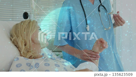 Healthcare worker in blue scrubs checking patient's pulse and preparing syringe in hospital room 135623509