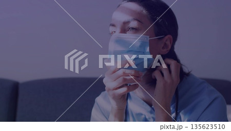 Adjusting worker wearing scrubs surgical mask in staff lounge with stethoscope on couch, copy space Adjusting worker wearing scrubs surgical mask in staff lounge with stethoscope on couch, copy space 135623510