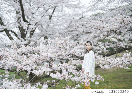 満開の桜を背景にして、笑顔の若い女性 満開の桜を背景にして、笑顔の若い女性 135623849