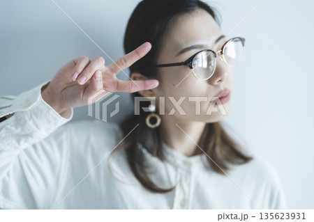 ピースサインをするメガネをかけた女性 135623931