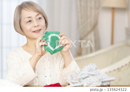 リビングで毛糸のアクリルたわしを編むシニア女性 135624322