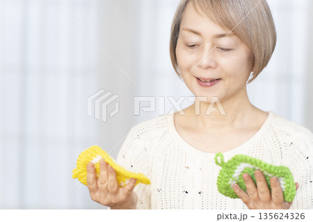 リビングで毛糸のアクリルたわしを編むシニア女性 135624326