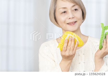 リビングで毛糸のアクリルたわしを編むシニア女性 135624328