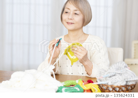リビングで毛糸のアクリルたわしを編むシニア女性 135624331