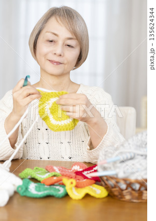 リビングで毛糸のアクリルたわしを編むシニア女性 135624344