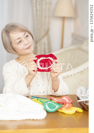 リビングで毛糸のアクリルたわしを編むシニア女性 135624352