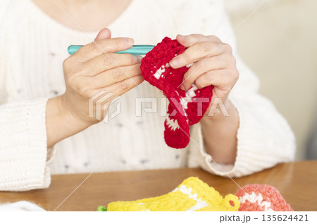 リビングで毛糸のアクリルたわしを編むシニア女性の手元アウトフォーカス 135624421