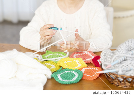 リビングで毛糸のアクリルたわしを編むシニア女性の手元アウトフォーカス 135624433