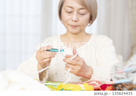 リビングで毛糸のアクリルたわしを編むシニア女性の手元アウトフォーカス 135624435