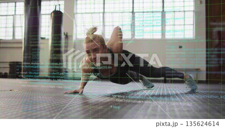 Trainer performing one-armed push-up variation in gym, with hex mat, heavy bag and code overlay 135624614