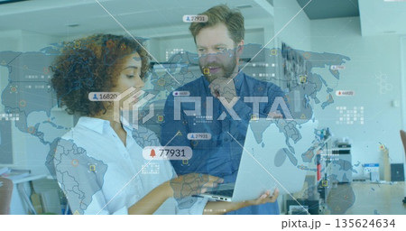 Colleagues wearing business wear reviewing laptop data in office, with analytics overlays 135624634