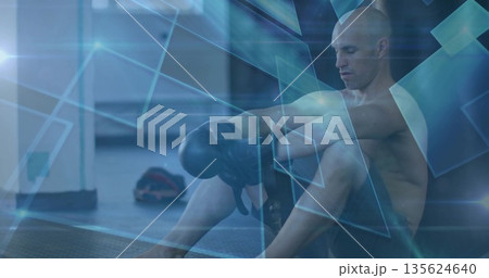 Adjusting boxing gloves athlete wearing black shorts on gym mat with geometric overlay, copy space 135624640