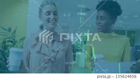Walking two colleagues carrying coffee cups and document folder in open office, with potted plant 135624656