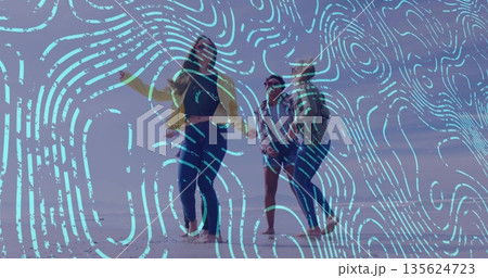 Three friends dancing barefoot on dusky beach, with yellow jacket, striped top and denim shorts Three friends dancing barefoot on dusky beach, with yellow jacket, striped top and denim shorts 135624723