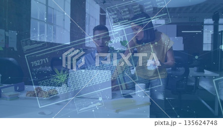 Reacting coworker noticing data overlay on laptop while colleague holding coffee mug in office 135624748