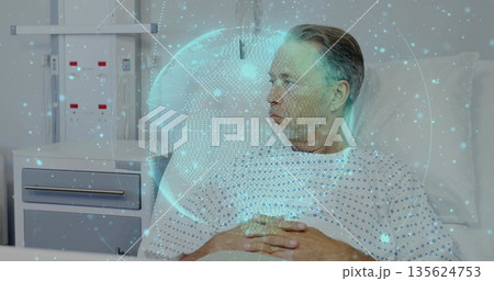 Senior patient lying in hospital bed, wearing gown, with holographic globe and IV stand, copy space 135624753