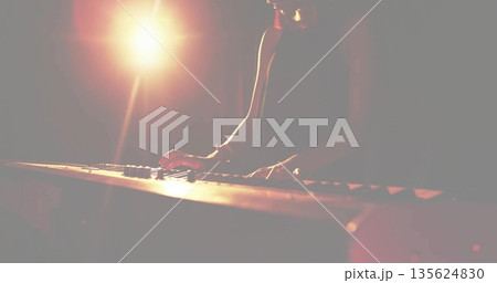 Female musician wearing sleeveless top playing electric keyboard on dark stage, with spotlight 135624830