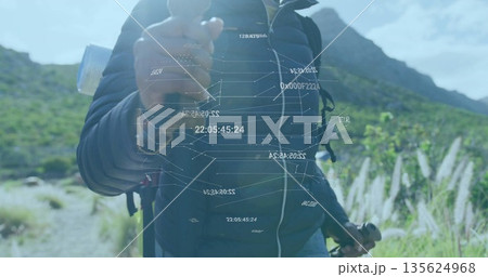 Manipulating floating data hologram, hiker in dark jacket on mountain trail with backpack and poles 135624968