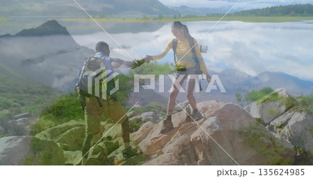 Hiking couple climbing rocky ledge beside calm mountain lake shore, with backpacks and hiking boots Hiking couple climbing rocky ledge beside calm mountain lake shore, with backpacks and hiking boots 135624985